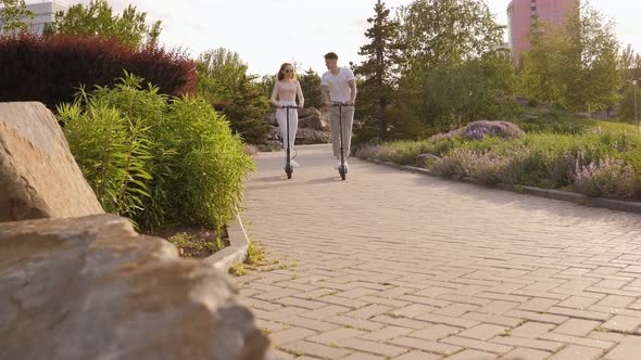 Happy Funny Teenagers Ride Electric Scooters in the Summer in the Park alt