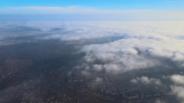 Aerial View From High Altitude of Distant City Covered with Puffy Cumulus Clouds Flying By Before alt