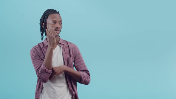 Tense Black Man with Dreadlocks Rubs Hand on Chin and Sighs Wearily Standing on a Blue Studio alt