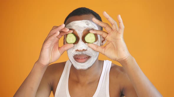 Portrait of a Positive African Guy with a Cosmetic Mask on His Face and Cucumber Slices, Isolated alt
