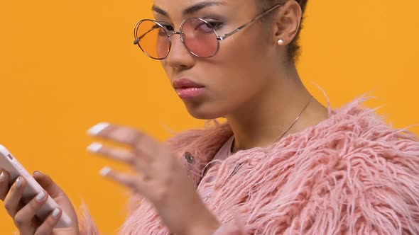 Glamorous Chic Female Typing Message on Smartphone, Looking Annoyed Into Camera alt