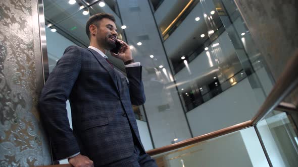 Joyful Businessman Talking on Phone in Lift Cabin alt