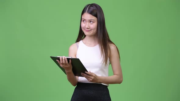 Young Beautiful Asian Businesswoman Holding Clipboard and Thinking
