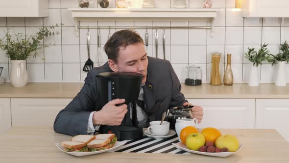 Sleepy Businessman Hugs Coffee Machine in Kitchen alt