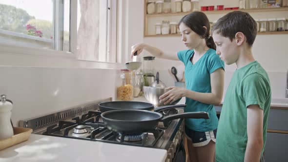 Young kids preparing pancakes in the kitchen using a frying pan alt
