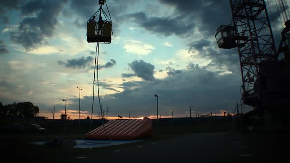 Silhouettes of People Going Down on Crane Platform at Dusk, Construction Site alt