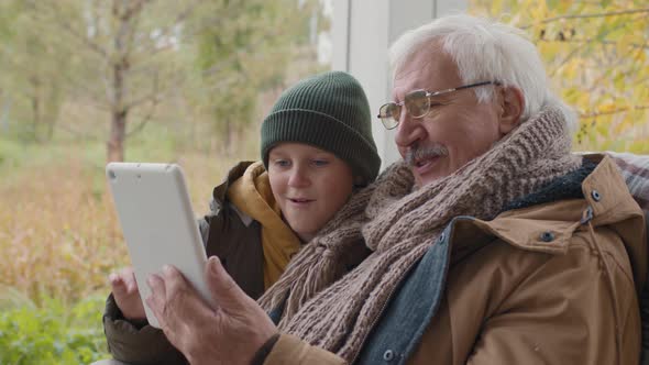 Child and Grandfather Sitting on Terrace and Using Tablet alt