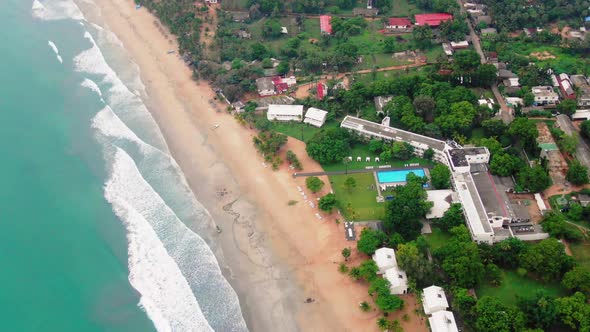 Aerial, tilt drone shot over waves and sand, on a paradise beach, towards buildings in Trincomalee c alt