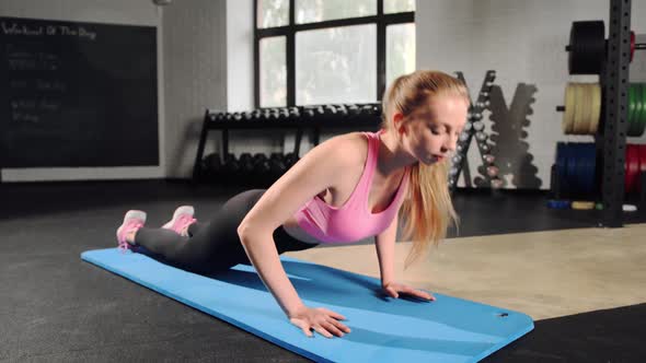 Young woman has workout at gym. Standing on knees and doing push ups with strong hands alt