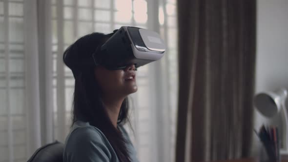 Happy Asian girl using 3D virtual reality headset at home.