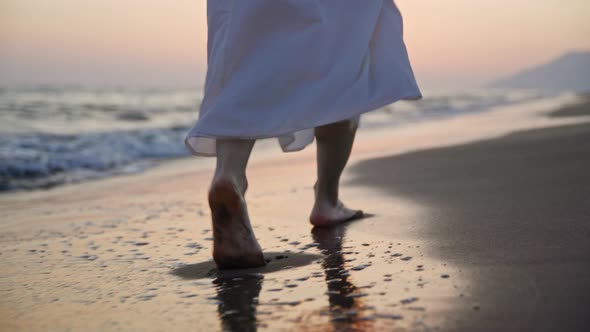 Young barefoot girl in a summer dress walking on the sand by the sea alt