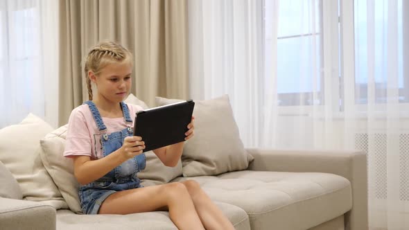 Preteen Child Playing Tablet and Listening to Music While Relaxing on Couch in Living Room at Home