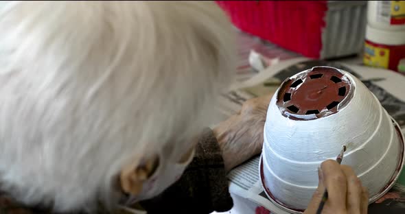 A tender grandma painting a flower pot as a hobby. Hand of an old woman holding a brush, close up alt
