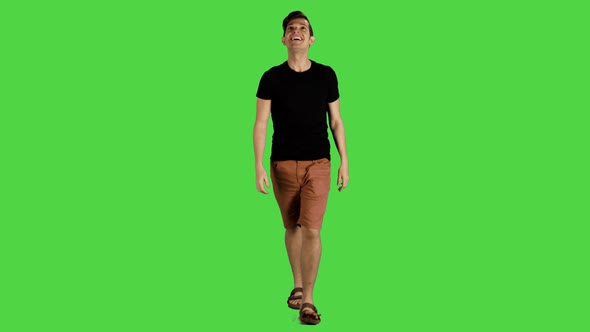 A young man smiling and looking around while walking over a green screen, 4k. alt