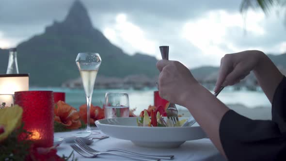A man and woman couple dining on the beach of a tropical island resort at sunset in Bora Bora. alt