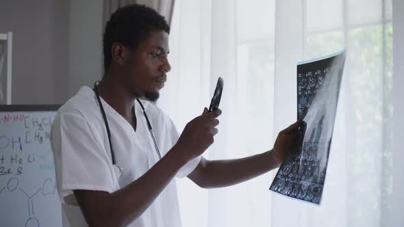 Side View Concentrated African American Radiologist Examining Brains Xray with Magnifying Glass alt