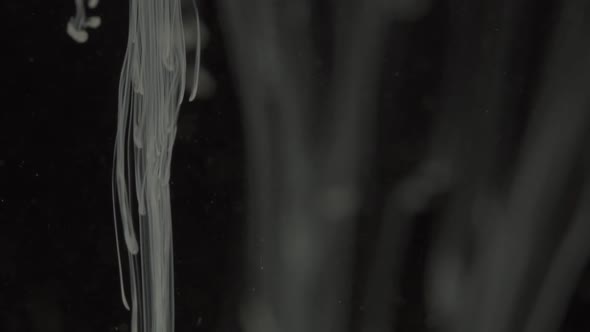 White liquiding on a dark background and forming different shapes. Macro shot, sideview. alt