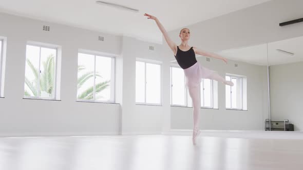 Caucasian female ballet dancer practicing ballet during a dance class in a bright studio alt