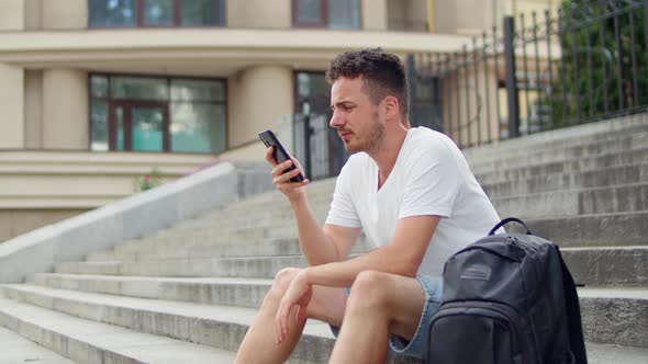 Handsome Young Man Sitting on the Steps of the Stairs in the City and Writing a Message on the alt