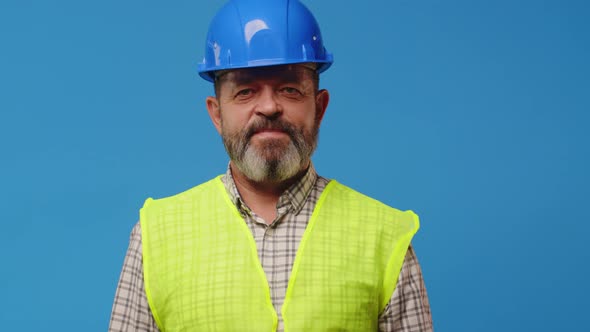 Smiling Senior Man Builder in Vest and Hardhat Against Blue Background