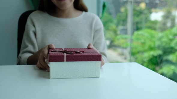 Closeup of a young woman receiving and opening a red present box