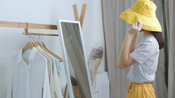Lovely Asian girl trying the new hat in front of the mirror. alt