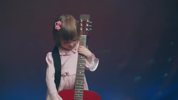 Little Girl in a Pink Vintage Dress Plays an Acoustic Guitar Like a Double Bass