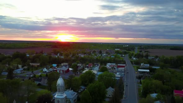 UHD aerial drone shot rising from behind a church to reveal a sunset over a small town alt