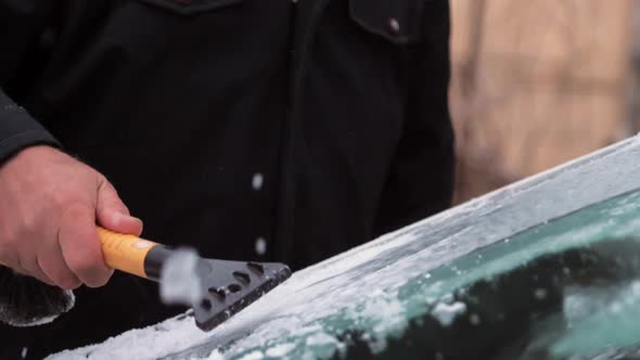 Person in Black Jacket Hands Clean Snow From Windshield alt