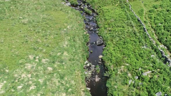 Wide-shot aerial birdseye view tracking forward over a river, with rocks and moorland surround. Dart alt