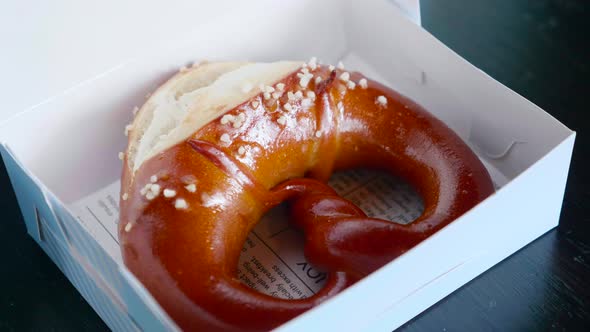 Close Up of Fresh Brown Pretzel with Sea Salt in White Paper Box in Pastry Shop alt