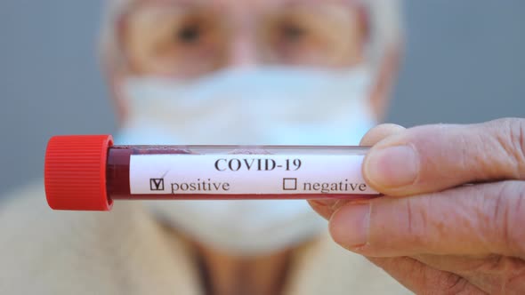 Elderly Woman with Protective Mask Holding Her Blood Test with Positive Result on Coronavirus. Sick alt