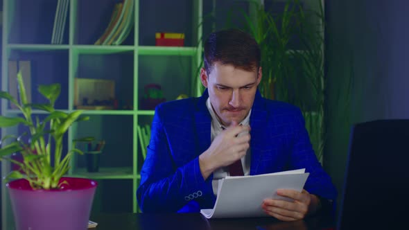 Young Man Examines Documents Sitting in Office alt