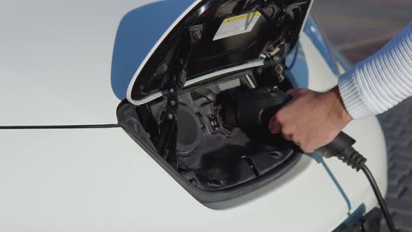 A Fairskinned Male Driver Connects Electric Car to Power System to Charge Car Battery alt