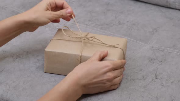 Hands of woman unwraps the gift, removing jute rope from gift box. Zero waste gift wrapping