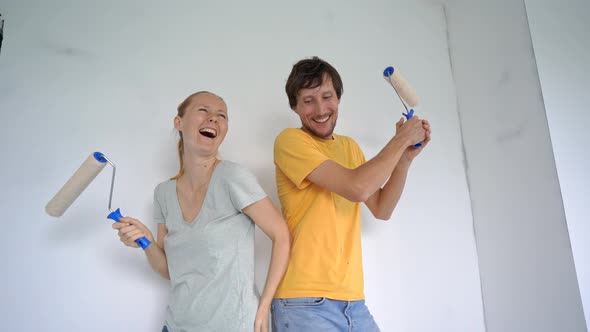 A Happy Man and Woman Paint the Wall Using a Roller Painter alt