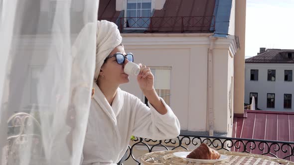 In Morning Woman In Bathrobe On Balcony Has Breakfast With Coffee And Croissant alt
