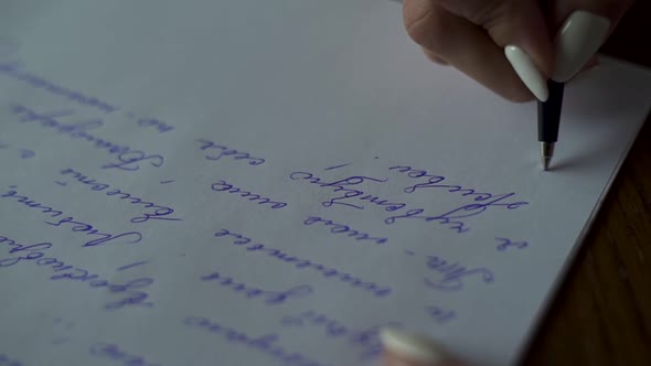 Female hands writing letter on white paper on wooden table close up. Сalligraphy brides vow