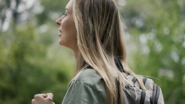 A Woman Drinks Water From a Bottle in the Forest alt
