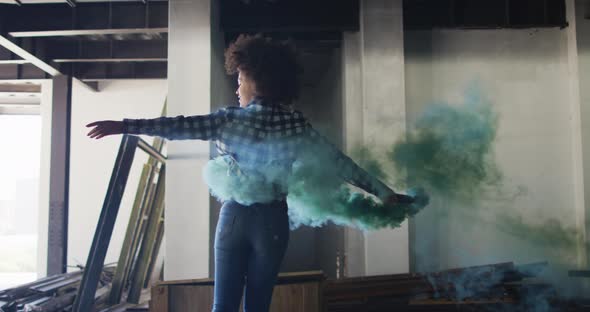 Mixed race woman holding green flare dancing in an empty building alt
