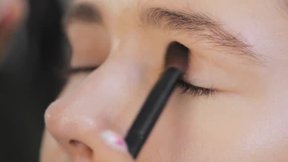Professional Makeup Artist Applying Eye Shadows To Upper Eyelid of Model Eyes
