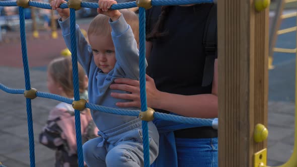 Mother Holds Son Trying to Climb on Metal Construction alt