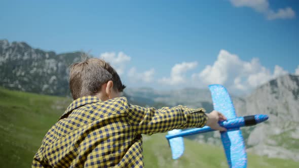 Happy little boy playing with a toy blue plane on a background of mountains in Montenegro alt
