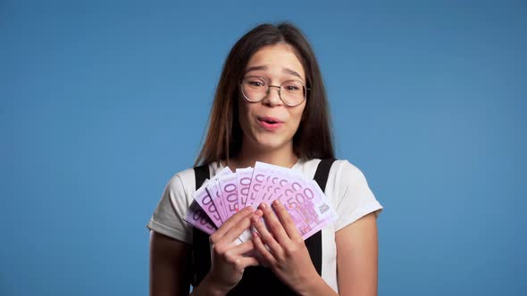 Satisfied Happy Excited Asian Girl Showing Money - Euro Currency Banknotes on Blue Wall. alt