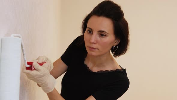 Woman making repairs at home, painting paint roller wall white paint. Renovation, family interior.