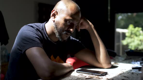 A casually dressed Asian man focused staring at his mobile phone on a counter table, the man waiting alt