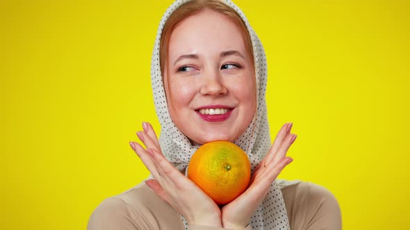 Closeup Portrait of Cheerful Redhead Caucasian Woman in Kerchief Holding Orange Fruit Looking at alt