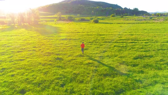 Flight Over Sport Man at Perfect Green Grass Meadow. Sunset in Mountain alt