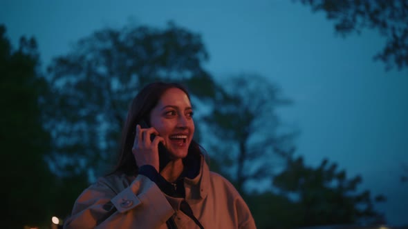 Young woman walks around in the evening city while enjoying a phone conversation alt
