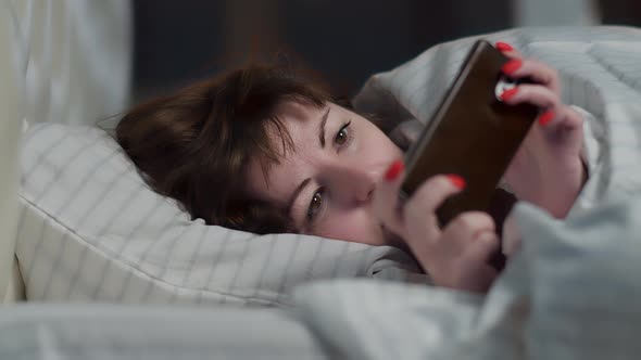 Sleepy Pretty Woman Lies on the Bed and Uses the Phone at Night Read Some Information